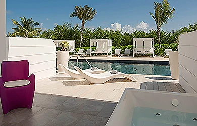 Piscina al aire libre con tumbonas y sillas, junto a palmeras y paredes blancas