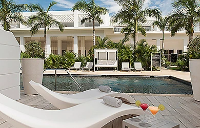 Piscina y tumbonas con palmeras frente a una villa blanca tropical
