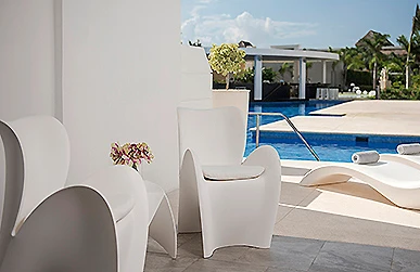 Vista de sillas blancas y piscina con cielo nublado al fondo.
