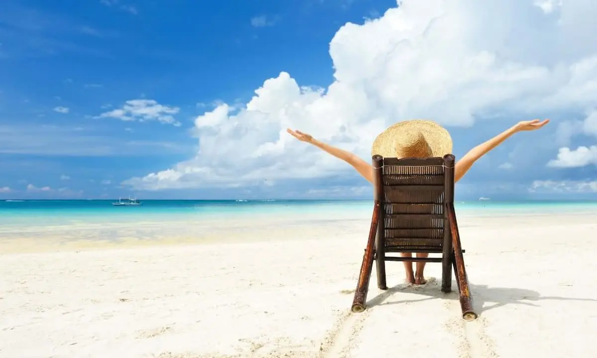 Silla de madera con sombrero en una playa paradis&iacute;aca bajo nubes y cielo azul.
