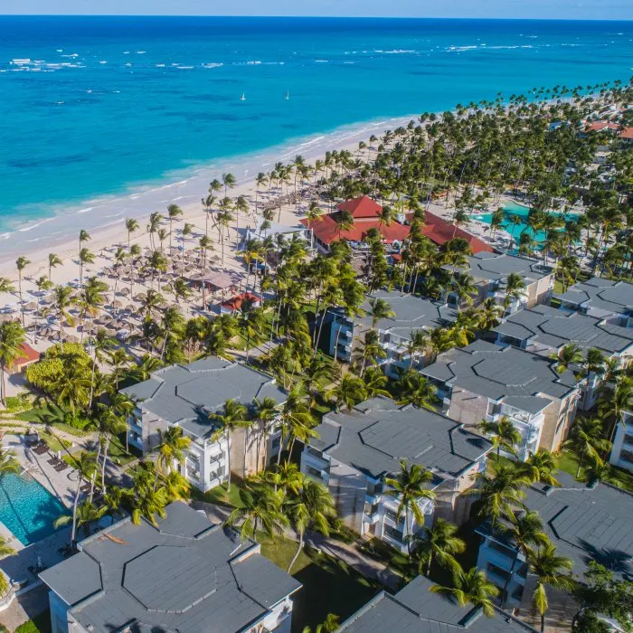 Vista a&eacute;rea de un hotel junto a playa tropical, palmeras y piscina.