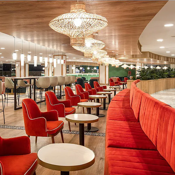 Sal&oacute;n moderno con sof&aacute;s rojos y mesas, l&aacute;mparas colgantes de mimbre.