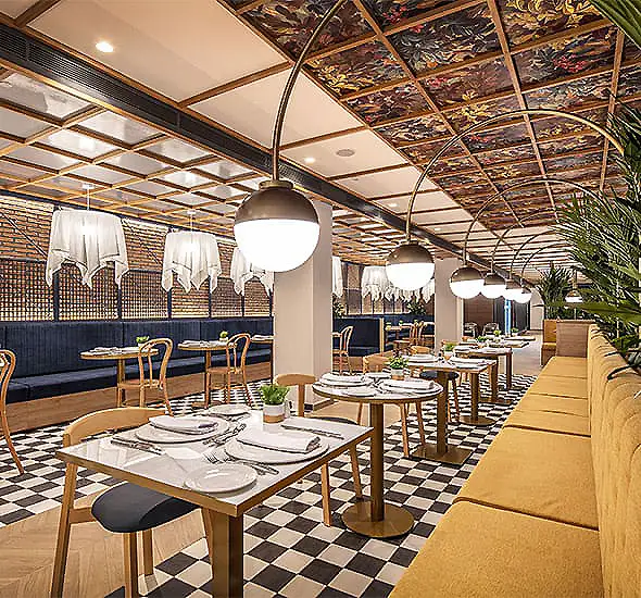 Comedor de restaurante con mesas, iluminaci&oacute;n colgante y techo decorado.