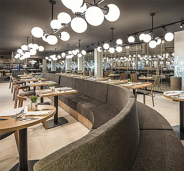 Sala de restaurante moderna con mesas, sof&aacute;s y luces colgantes redondas.