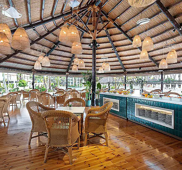Restaurante con mesas de mimbre, barra azul y l&aacute;mparas colgantes bajo techo de madera