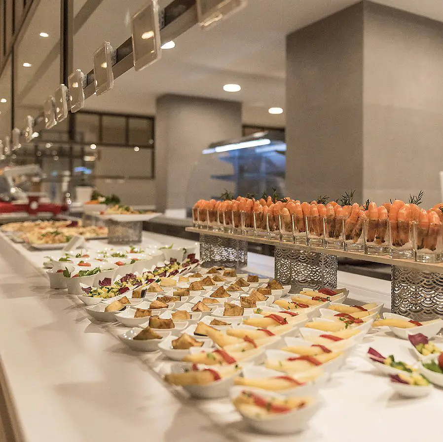 Mesa buffet con mini entrantes y brochetas de frutas en vasos, en un evento interior