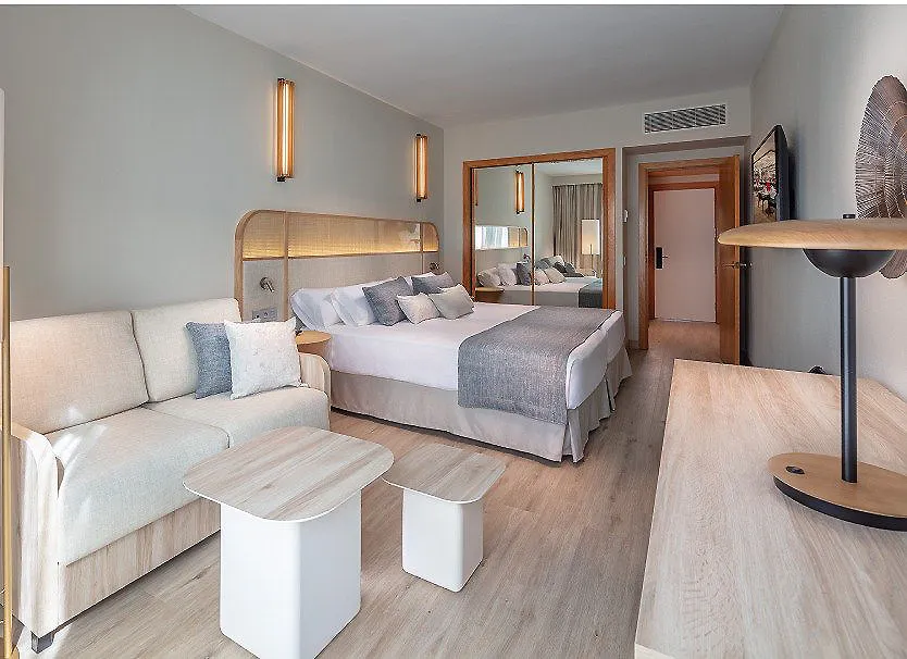 Suite hotelera moderna con cama doble, sof&aacute; y mesas auxiliares.