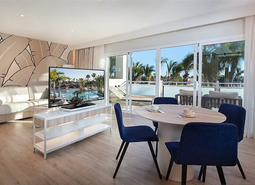 Sala comedor moderna con mesa y sillas azules, vista a la piscina y palmeras.