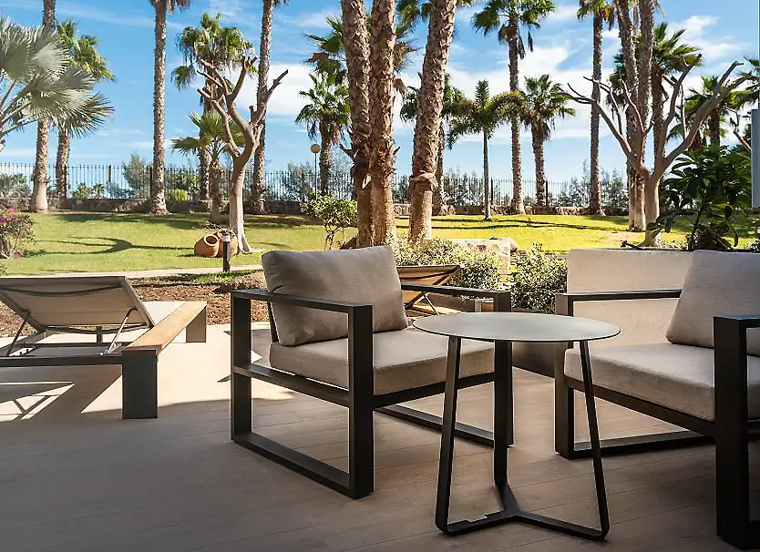 Terraza con muebles y jard&iacute;n tropical con palmeras bajo el cielo azul
