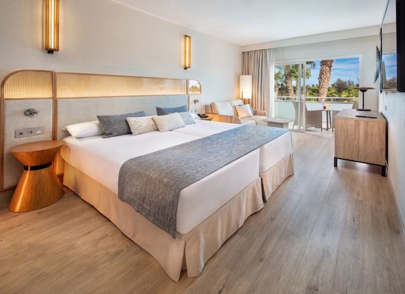 Habitaci&oacute;n de hotel moderna con cama doble y acceso a balc&oacute;n y TV.
