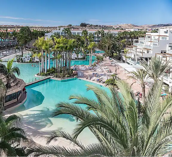 Piscina de hotel con palmeras y edificios blancos, vista panor&aacute;mica.