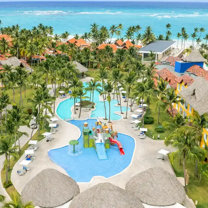 Hotel tropical con piscina y palmeras frente al mar.