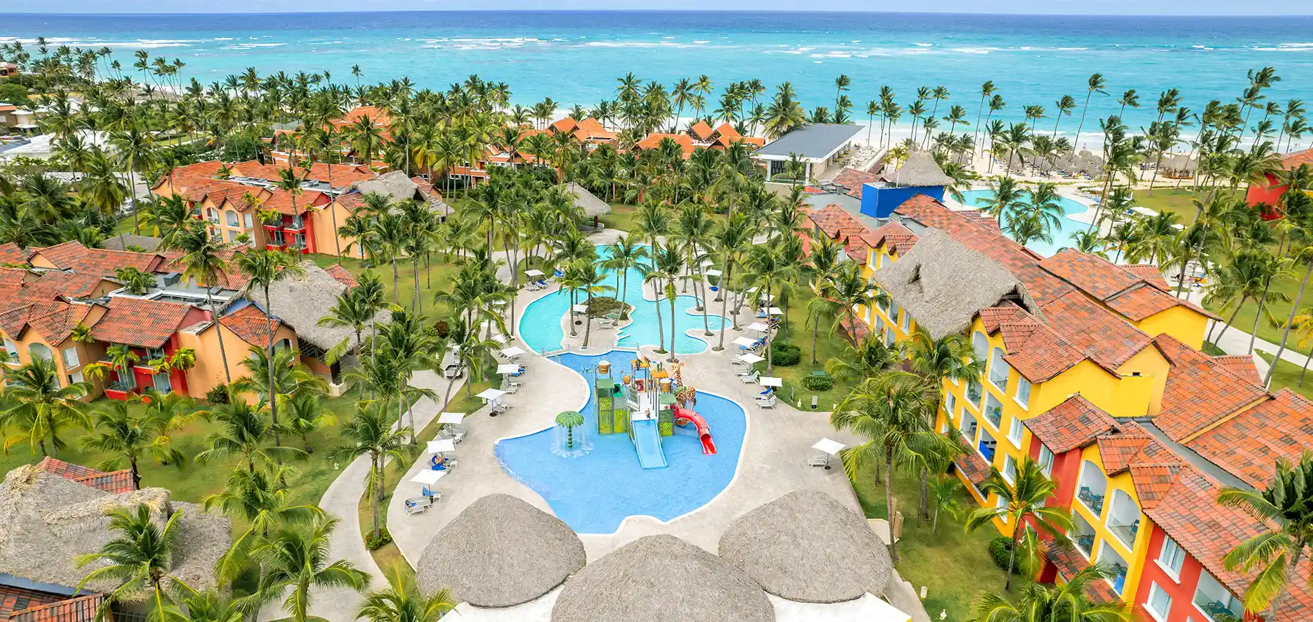 Vista a&eacute;rea de hotel con piscina, palmeras y mar turquesa al fondo