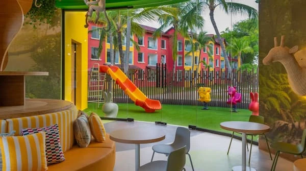 Parque infantil con tobog&aacute;n amarillo y colores en patio con palmeras.