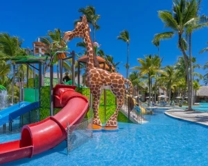 Jirafa de juguete junto a toboganes y piscina en resort con palmeras