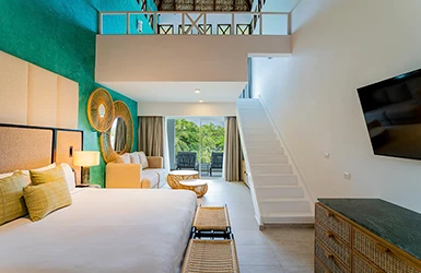 Interior de hotel con cama, sof&aacute;s, escaleras y jard&iacute;n al fondo