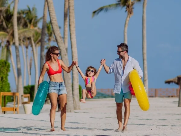 Familia en la playa jugando con flotadores de colores y el sol.
