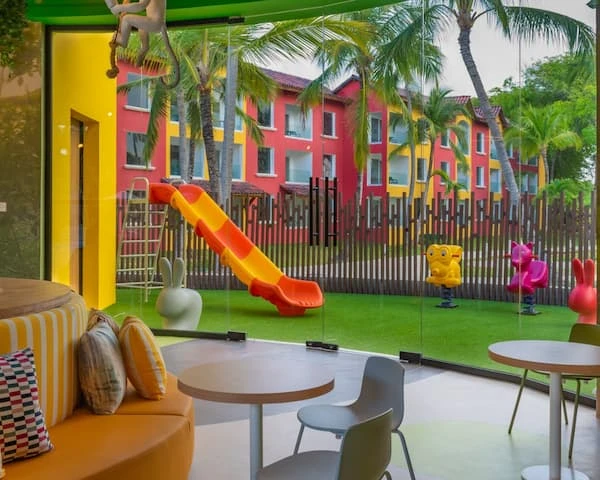 &Aacute;rea de juegos infantil con resbaladilla y palmeras junto a edificio pintado