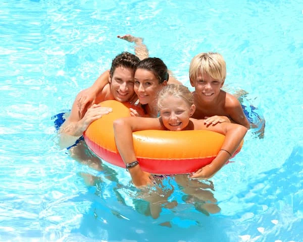 Familia en piscina sonriente con flotador naranja y azul, en el agua.