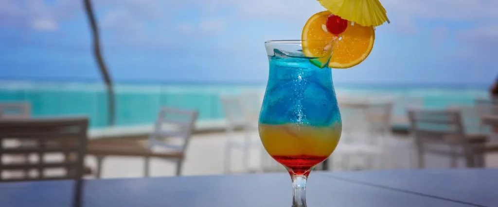 C&oacute;ctel azul con rodajas de naranja y limonada en la playa, vaso con sombrilla