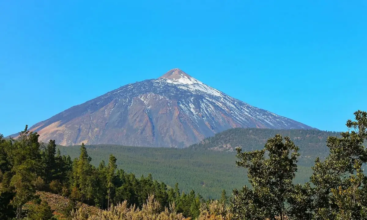 Monta&ntilde;a volc&aacute;nica con nieve en la cima y bosques alrededor bajo un cielo azul.