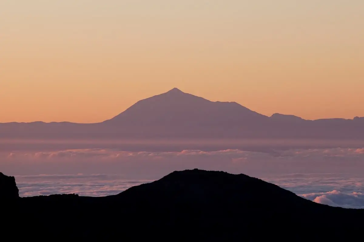 Monta&ntilde;as en silueta al atardecer con cielo rosado y nubes