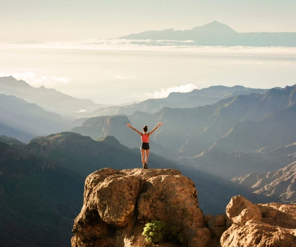 Persona en una roca mirando el valle y monta&ntilde;as al atardecer
