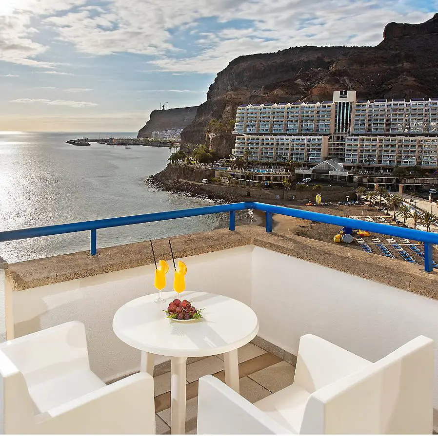 Terraza de hotel con mesa blanca, vista al mar y acantilado, colgando de palmeras