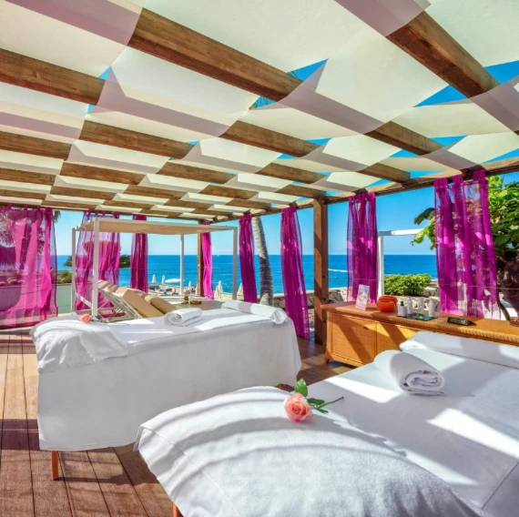 Camas de masaje en terraza frente al mar con toldo y cortinas fucsia