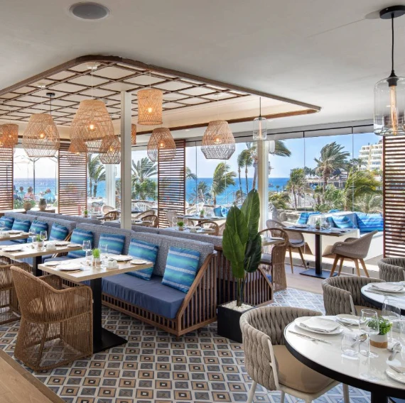 Comedor al aire libre con mesas azules y palmeras junto al mar
