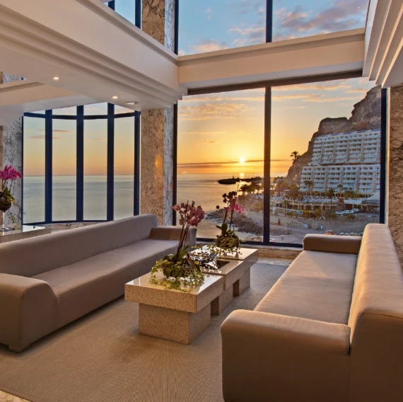 Terraza moderna con sof&aacute;s y vista al atardecer sobre el mar y el hotel