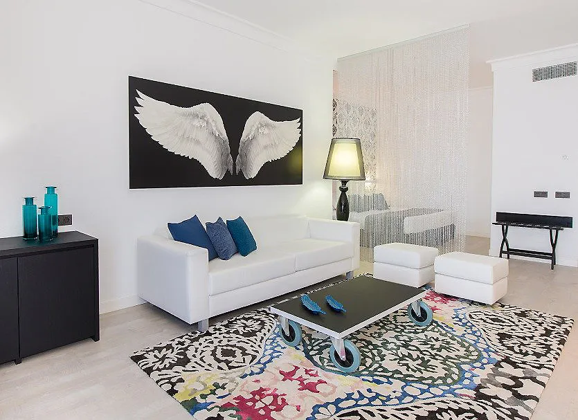 Sala moderna blanca con sof&aacute;, alfombra estampada y cuadro de alas de &aacute;ngel