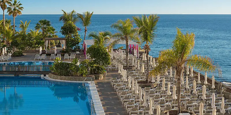 Piscina y fila de sillas con palmeras frente al mar azul.