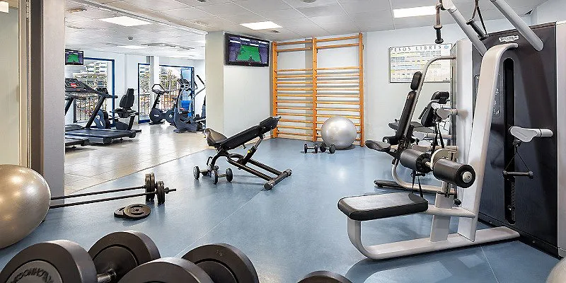 Gimnasio con m&aacute;quinas de ejercicio, mancuernas y bal&oacute;n suizo en el suelo