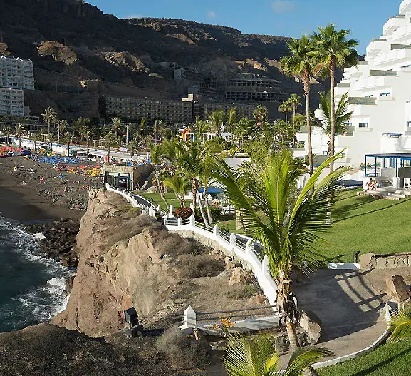 Acantilado con palmeras y paseo junto a un hotel, playa y costa rocosa.