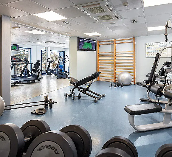 Gimnasio con m&aacute;quinas, pesas y bancos, sala de entrenamiento con luz blanca
