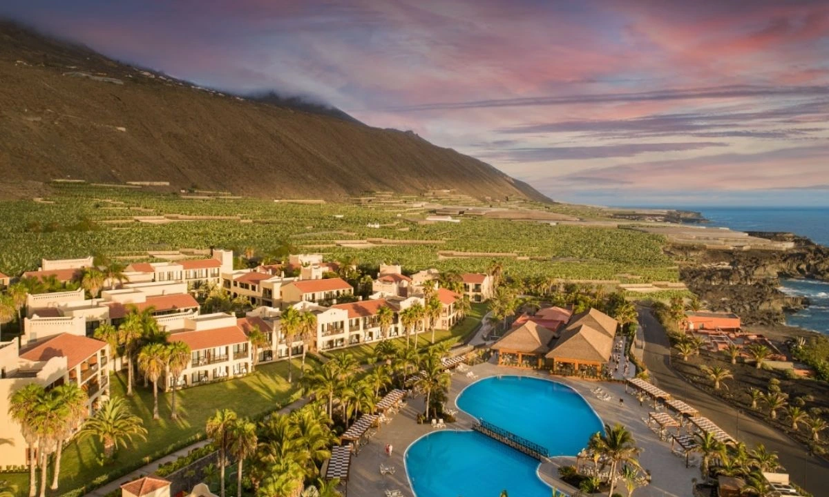 Aerial view of Esencia de La Palma at the La Palma Princess hotel, with blue pools, banana plantations and cliffs at sunset.