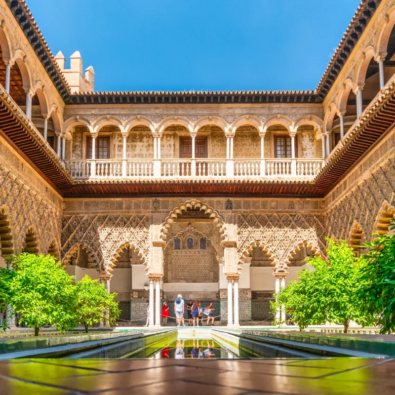 Patio interior con arcos y piscina reflectante, rodeado de vegetaci&oacute;n.