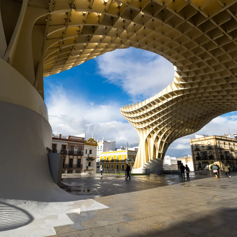 Estructura arquitect&oacute;nica moderna con cielo azul y nubes, gente caminando alrededor.