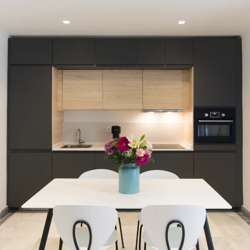 Cocina moderna con mesa, sillas blancas y jarr&oacute;n con flores.