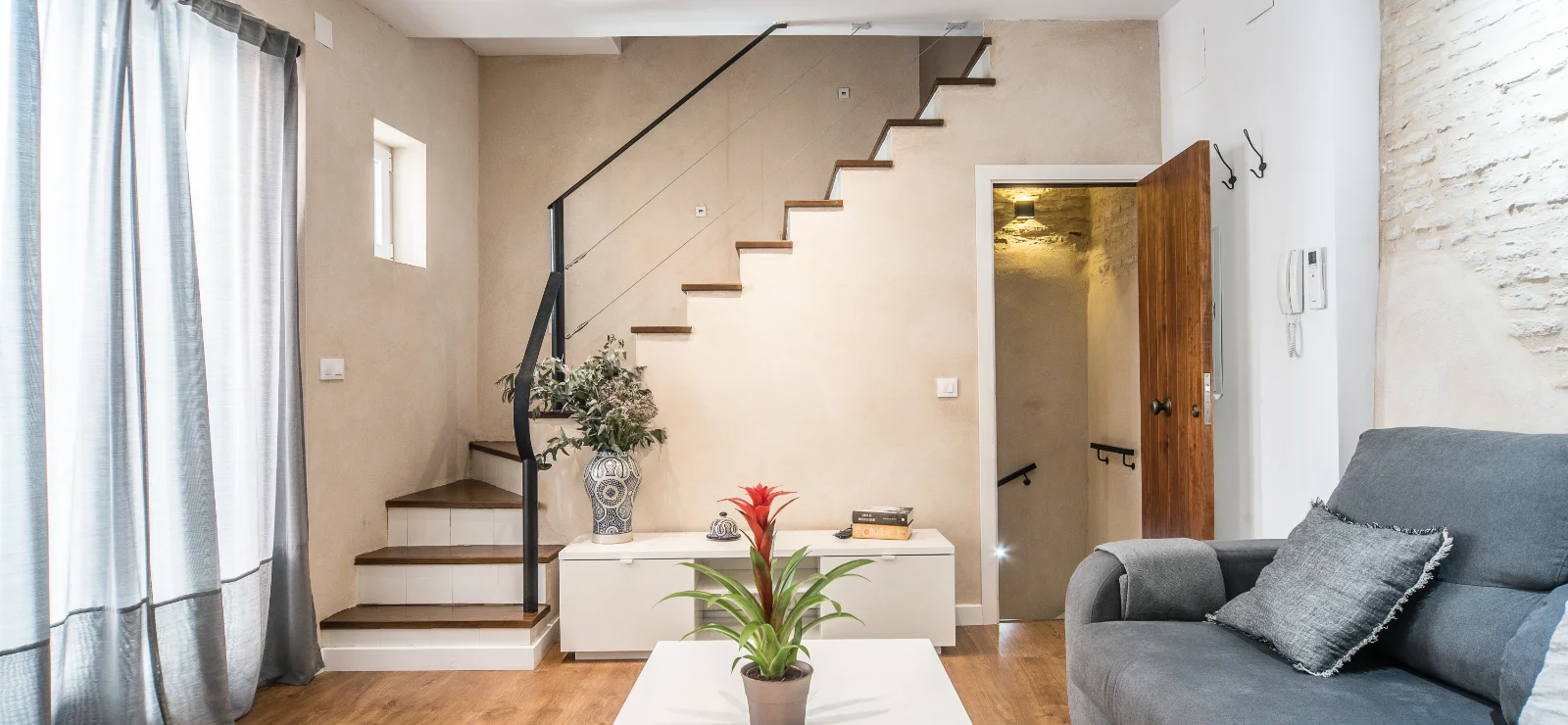 Sala moderna con escalera, sof&aacute; gris y planta sobre mesa.