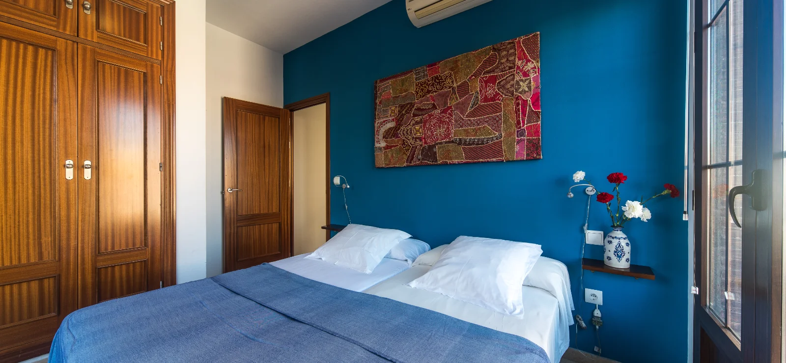 Habitaci&oacute;n con cama doble, pared azul, y puerta y armarios de madera.