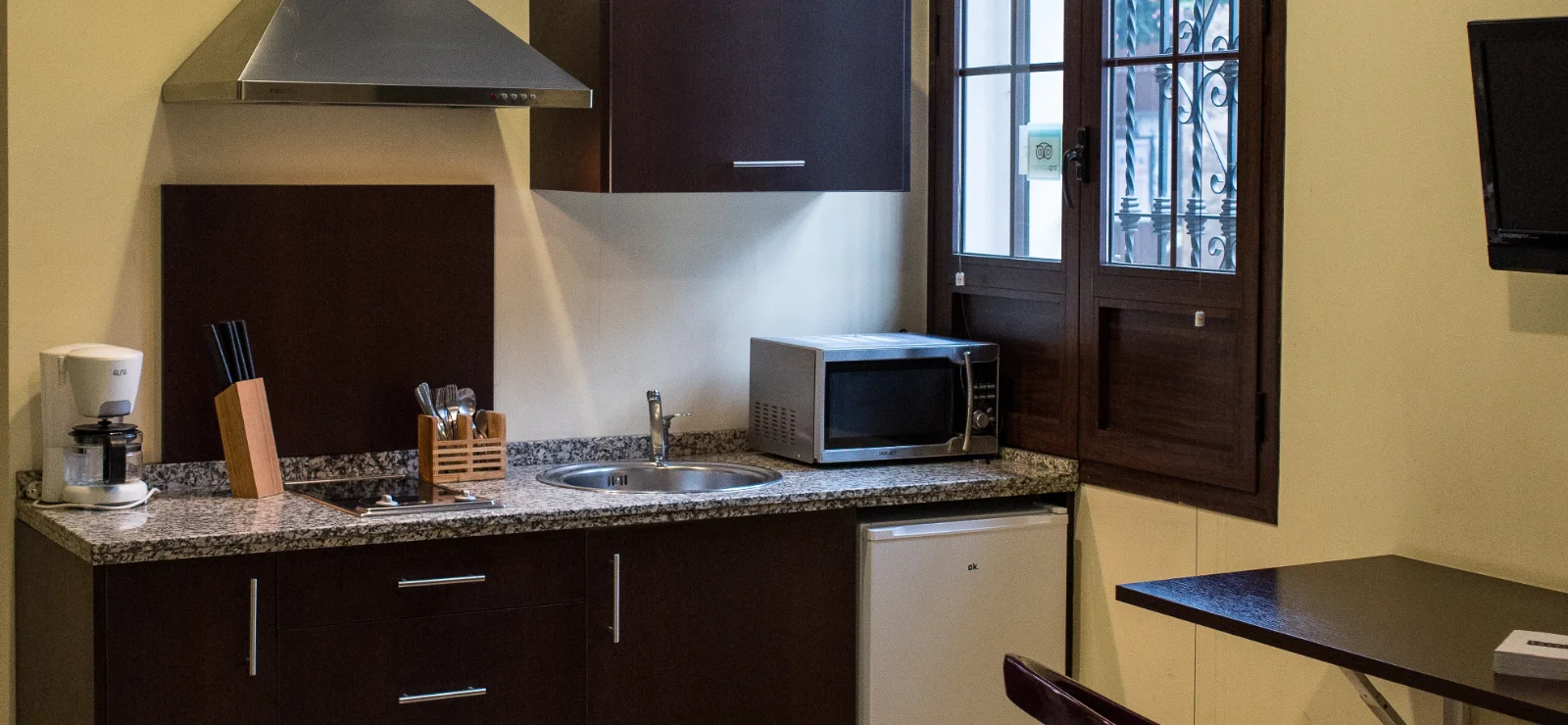 Cocina compacta con microondas, cafetera y ventana con vista.