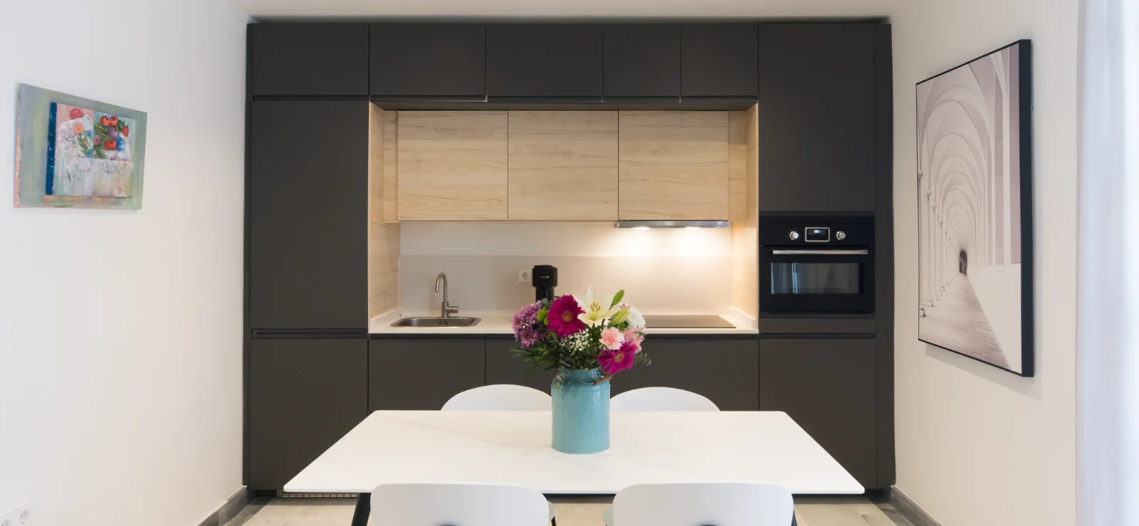 Cocina moderna con mesa blanca y jarr&oacute;n de flores.
