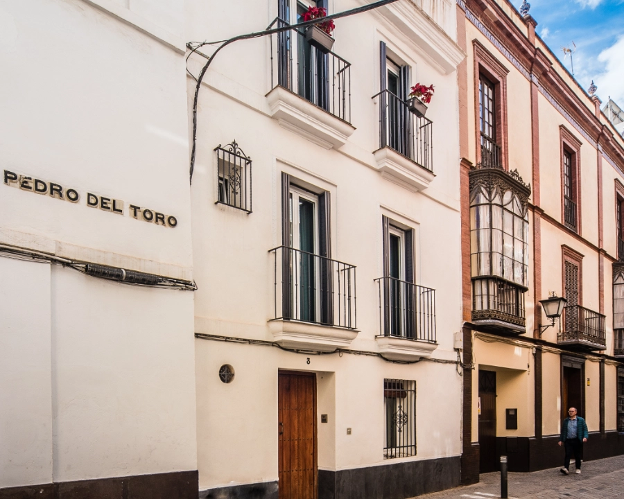 Calle estrecha con fachadas blancas y balcones, hombre caminando.