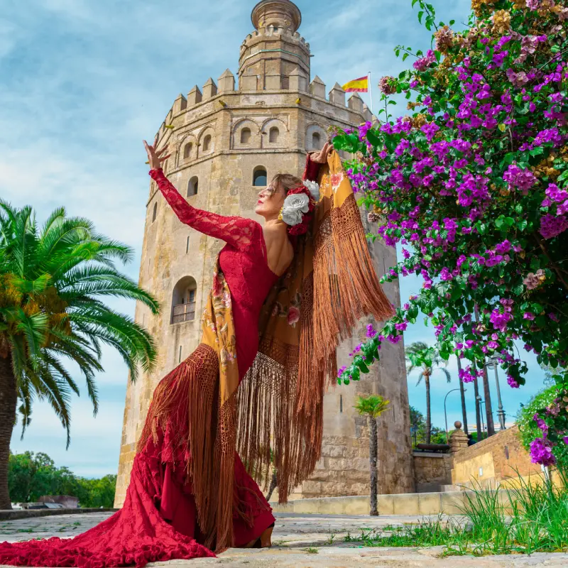 Bailarina de flamenco en traje rojo junto a la Torre del Oro y flores.