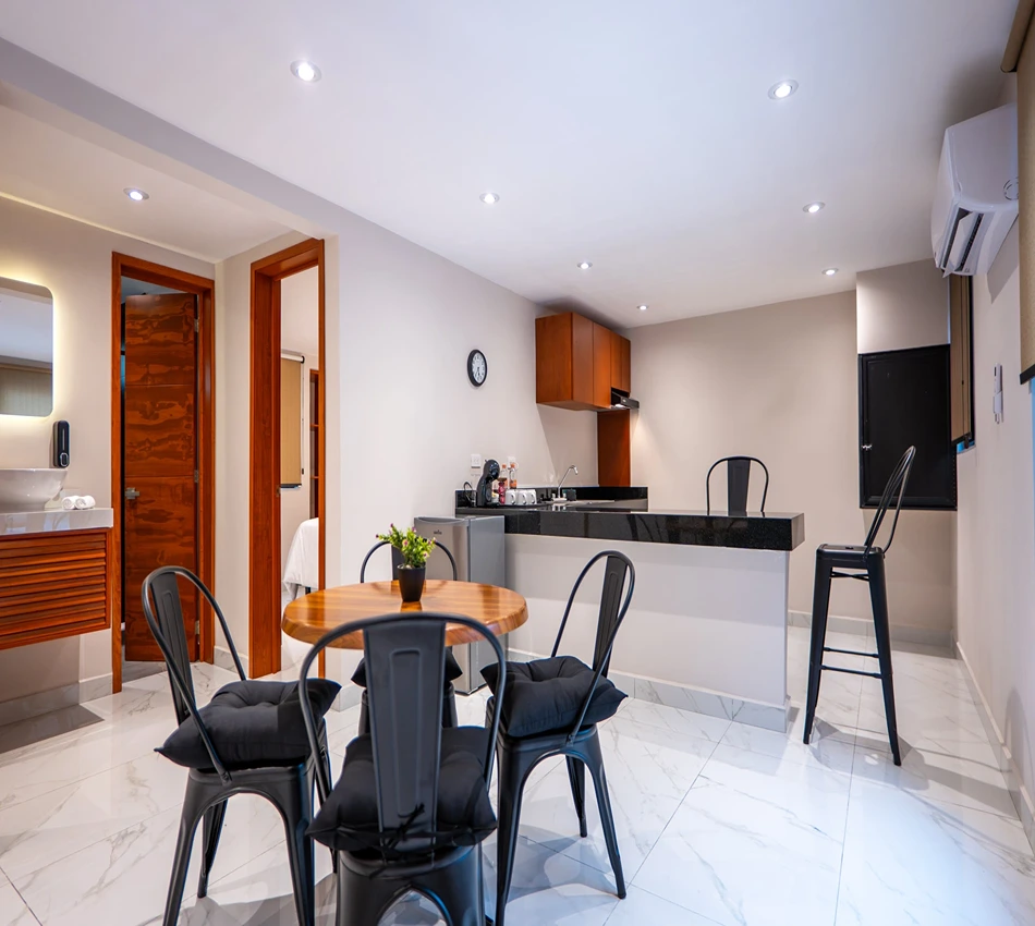 Sala moderna con cocina, mesa y sillas negras, y luz c&aacute;lida.