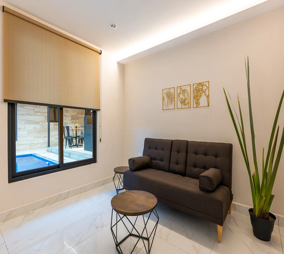 Sala moderna con sof&aacute;, mesa y planta, ventana con vista al exterior y piscina.