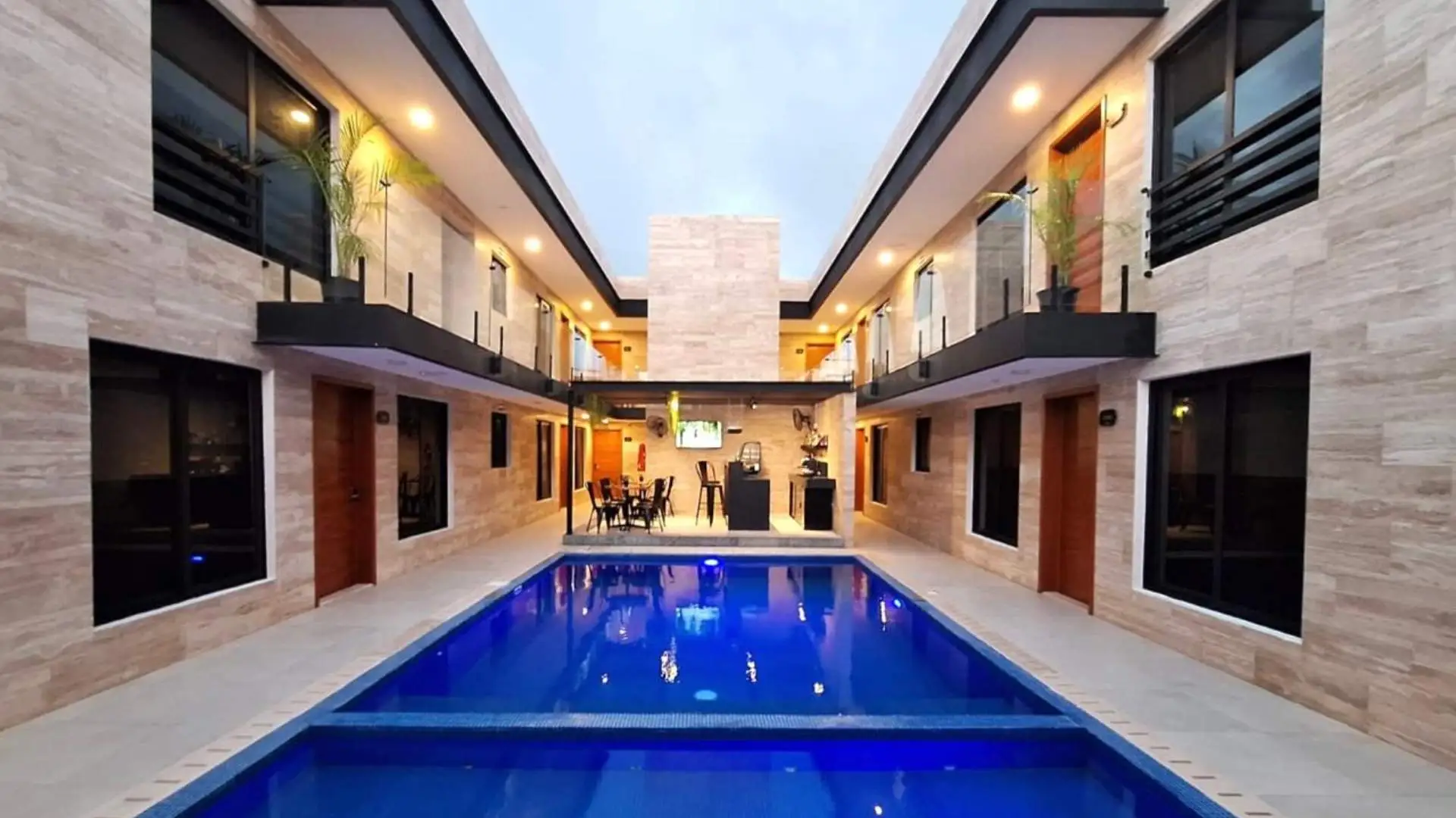 Patio con piscina azul rodeado de paredes de piedra beige y balcones con plantas.