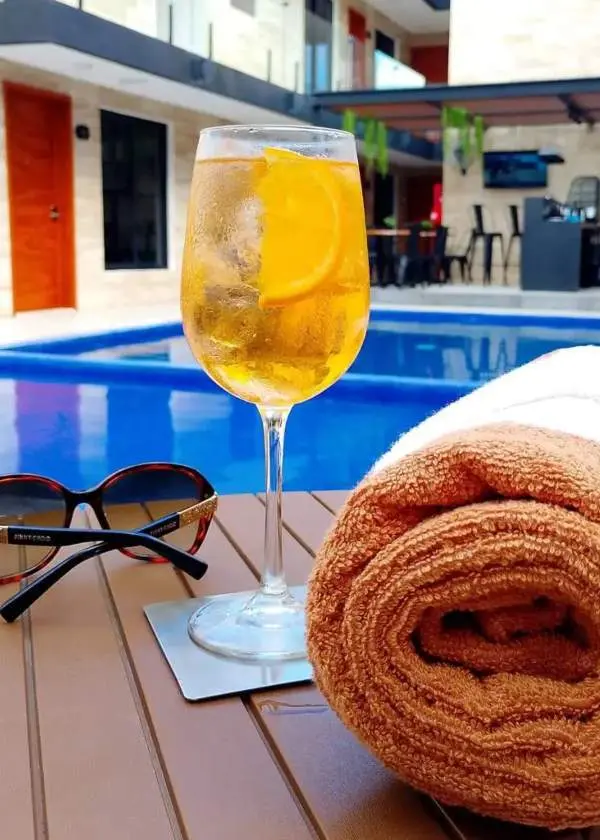 Mesa con gafas de sol, copa de cerveza y toalla con piscina de fondo